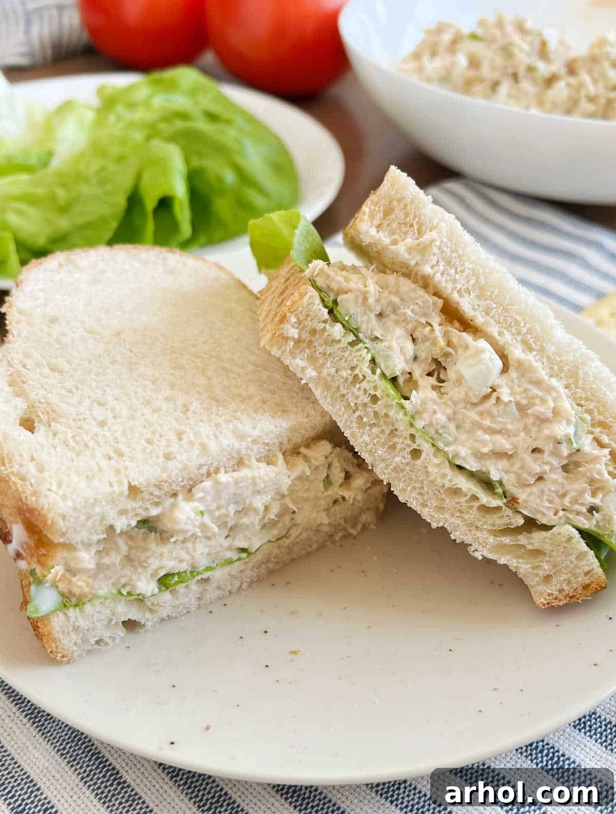 A classic tuna salad sandwich, beautifully presented on sourdough bread with fresh lettuce and ripe tomato slices, offering a timeless and satisfying meal.