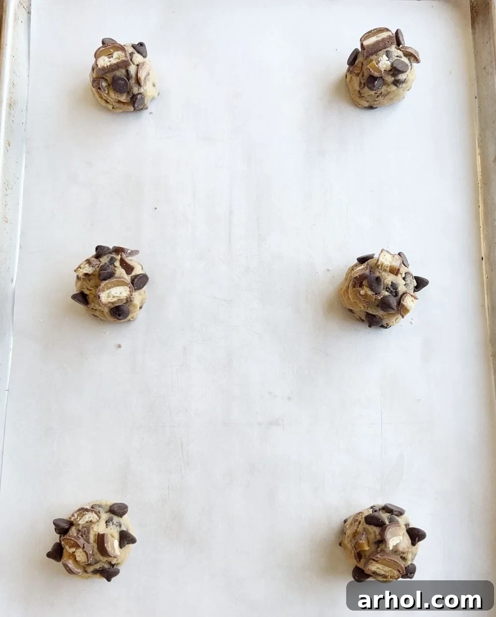 Rows of perfectly scooped, chilled cookie dough balls dotted with chocolate chips on a baking sheet lined with parchment paper.