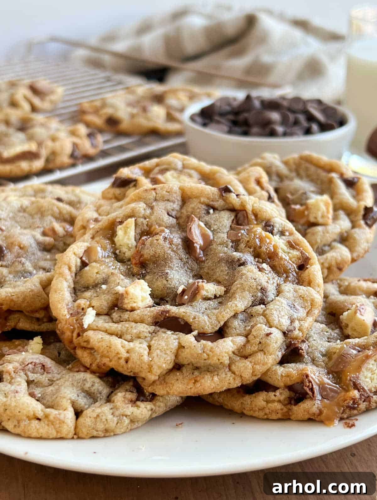 Close-up of a plate filled with warm, chewy chocolate chip cookies, each generously studded with chopped Twix bar pieces and melted chocolate morsels.