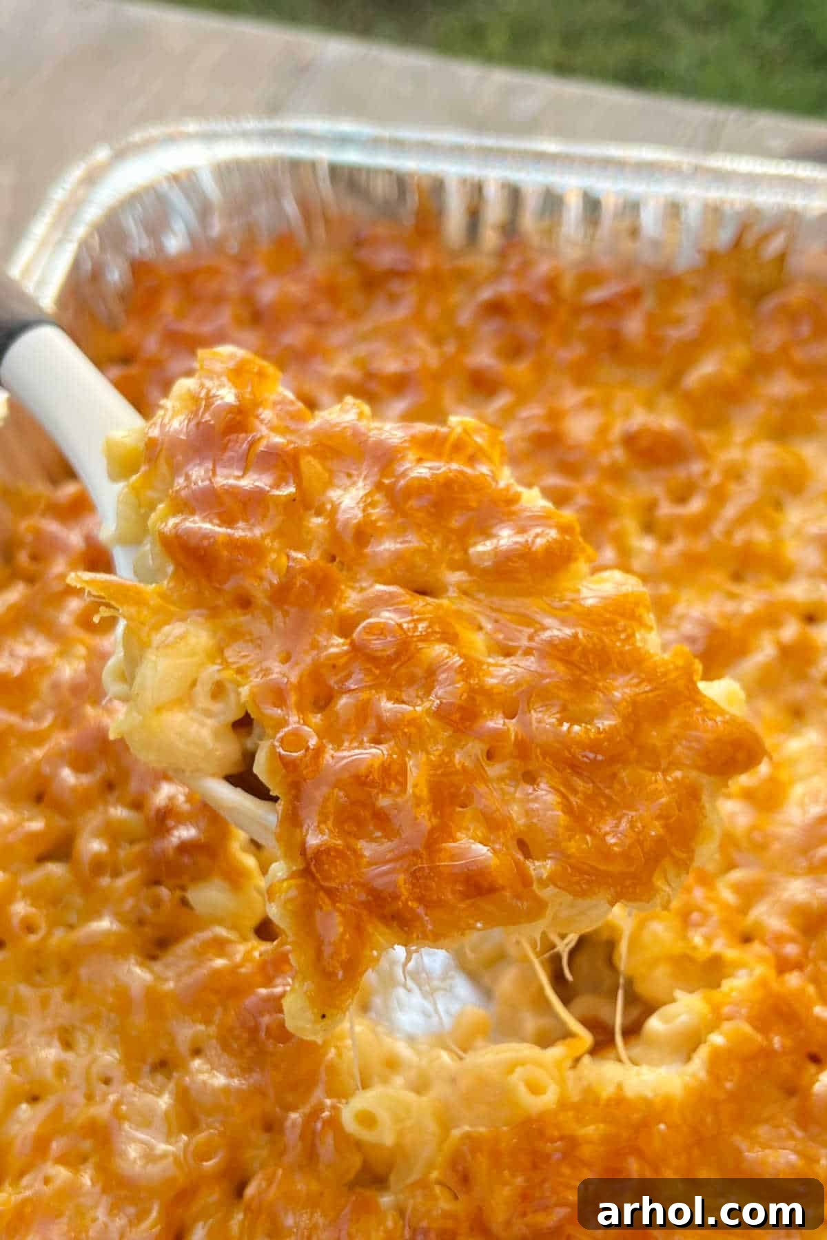 A serving spoon lifting a generous portion of creamy smoked mac and cheese, showing its golden crust and melted cheese pull.