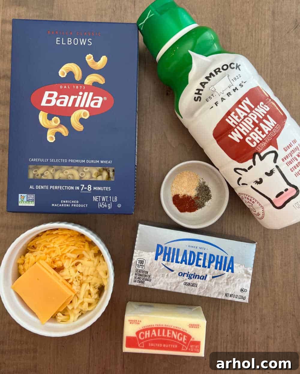 Raw ingredients for smoked mac and cheese laid out: elbow macaroni, heavy cream, various seasonings, cream cheese, butter, and a selection of cheeses.