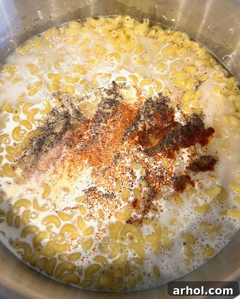 Elbow macaroni cooking in a pot with heavy cream and various seasonings, creating a rich base for the cheese sauce.