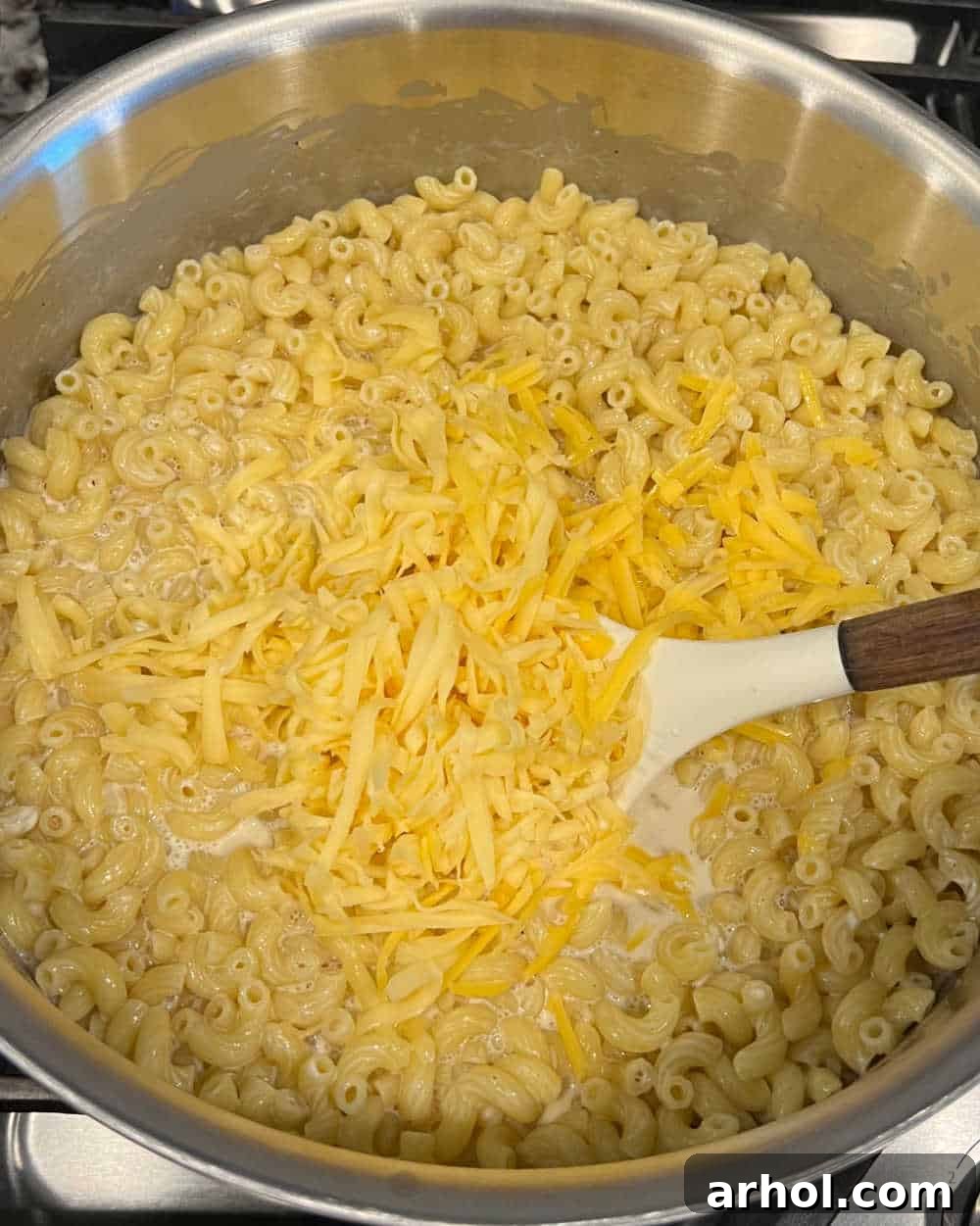 A large pot of cooked elbow macaroni being stirred with melted cheese and creamy sauce, forming a smooth, rich mixture.
