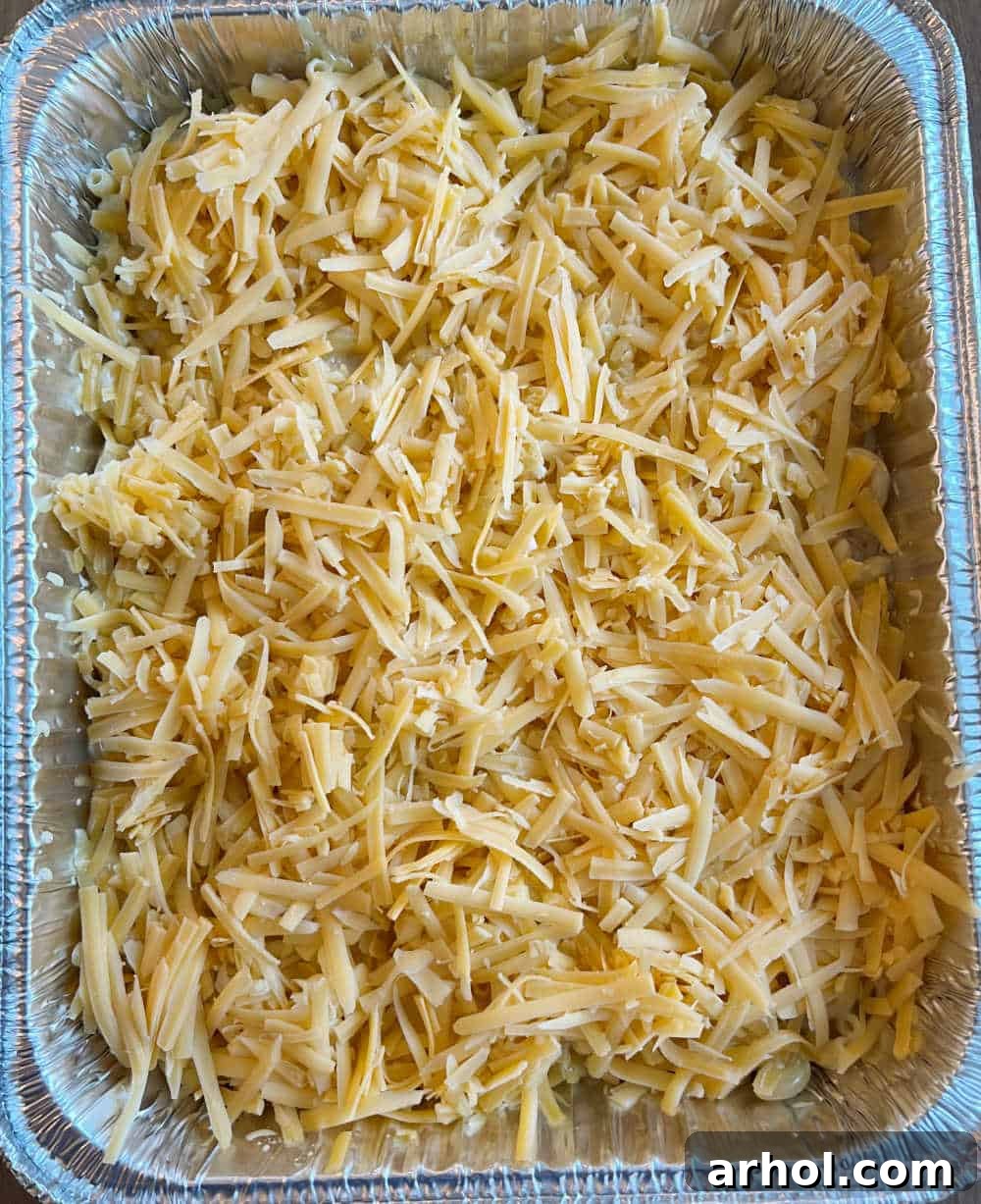 A foil pan filled with macaroni and cheese, generously topped with an extra layer of shredded cheese, ready to be placed in the smoker.