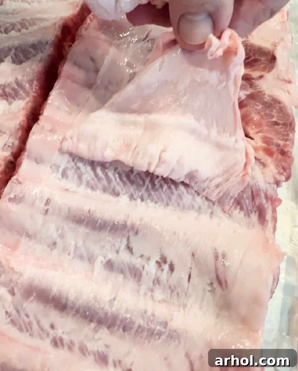 Close-up view of a hand expertly pulling the membrane off the back of a rack of ribs.