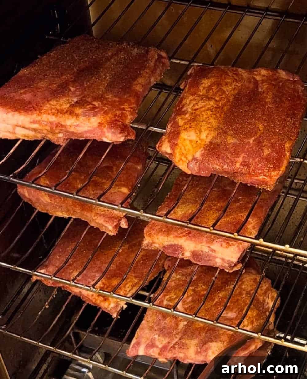 Two racks of seasoned ribs resting on the racks inside an electric smoker, bone-side down.