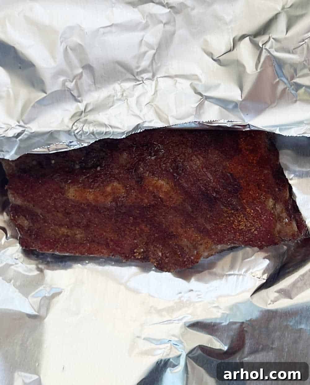 Racks of smoked ribs tightly wrapped in aluminum foil, ready for the next phase of cooking.