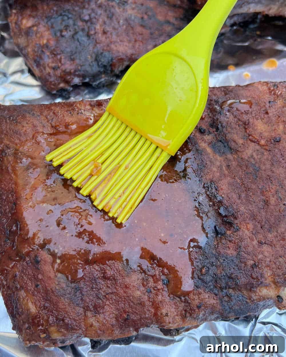 A basting brush applying generous amounts of BBQ sauce to smoked ribs inside an electric smoker.