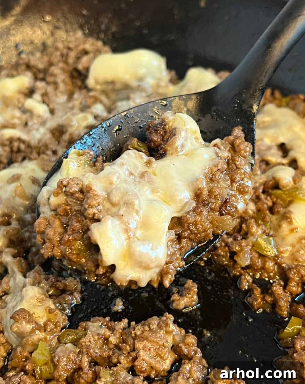 Cheesesteak sloppy joe meat mixture with gooey melted cheese being scooped with a spoon.