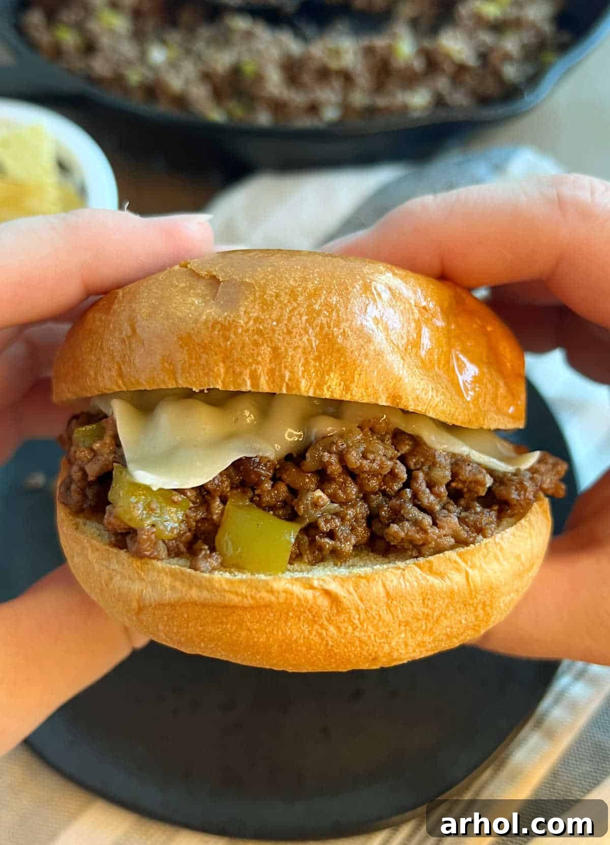 A Philly Cheesesteak Sloppy Joe sandwich on a toasted bun held in hand, showing the rich filling and melted cheese.