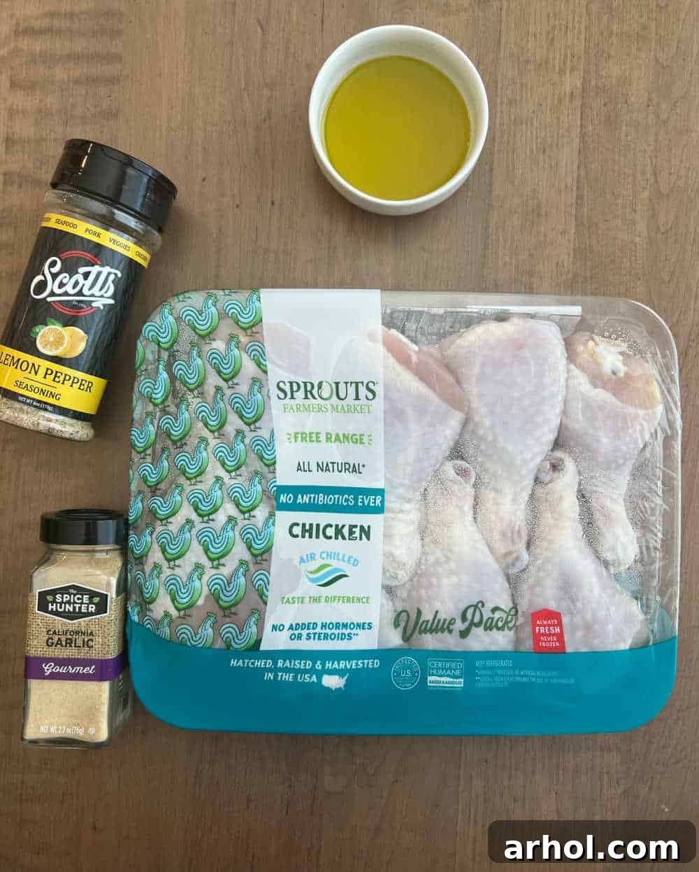A visual display of the simple ingredients needed for this recipe: a package of fresh chicken legs, a bottle of olive oil, a shaker of garlic powder, and a container of lemon pepper seasoning.