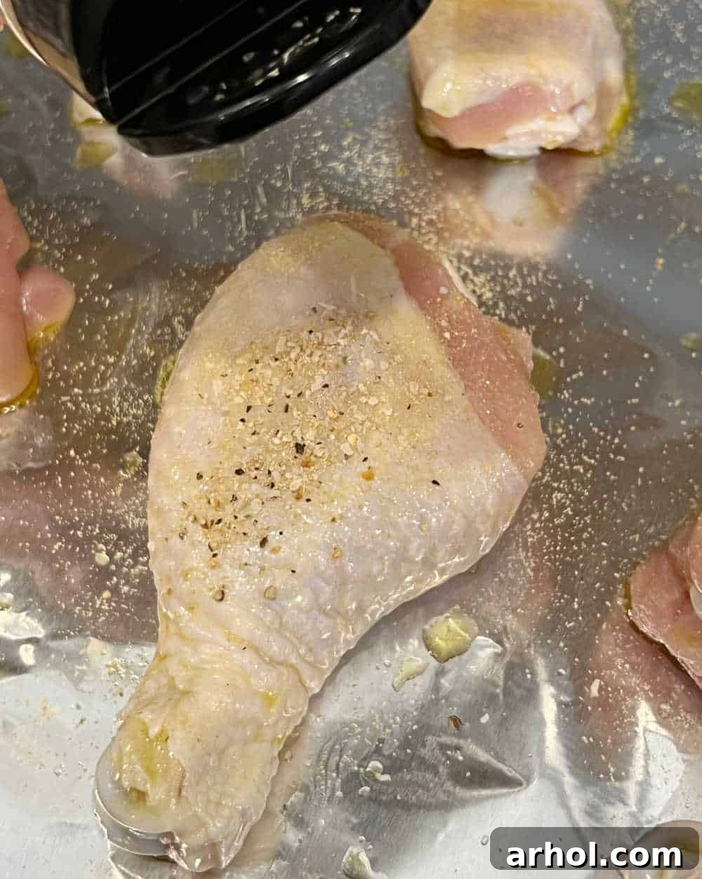 Raw chicken drumsticks generously seasoned with lemon pepper and garlic powder on a baking sheet, ready for the oven.