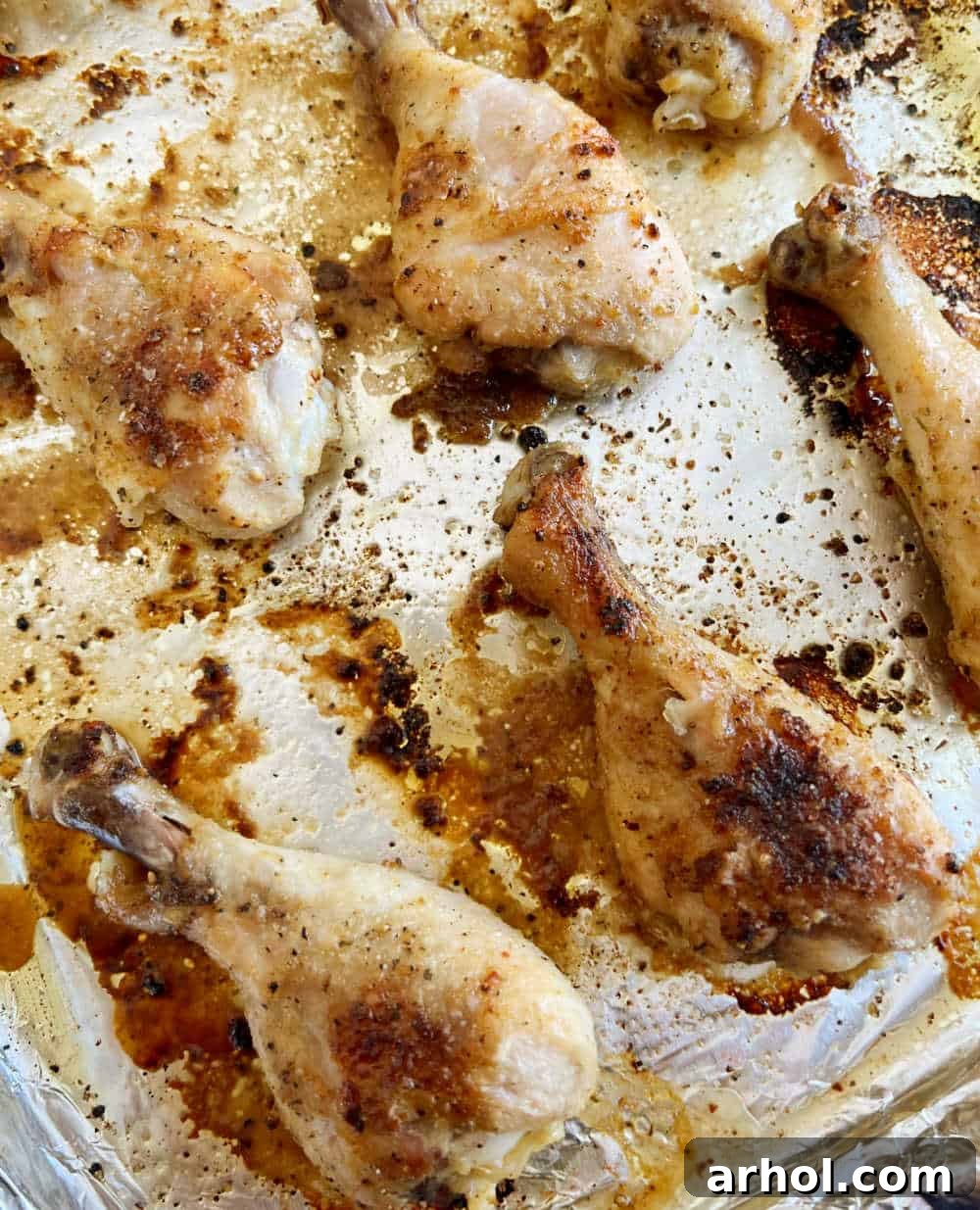Golden brown and crispy oven-baked chicken drumsticks cooling on a foil-lined baking sheet, fresh out of the oven.
