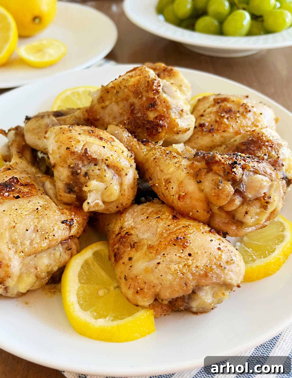 A beautifully arranged plate of golden oven-baked chicken legs, garnished with fresh lemon slices, placed on a rustic dining table.