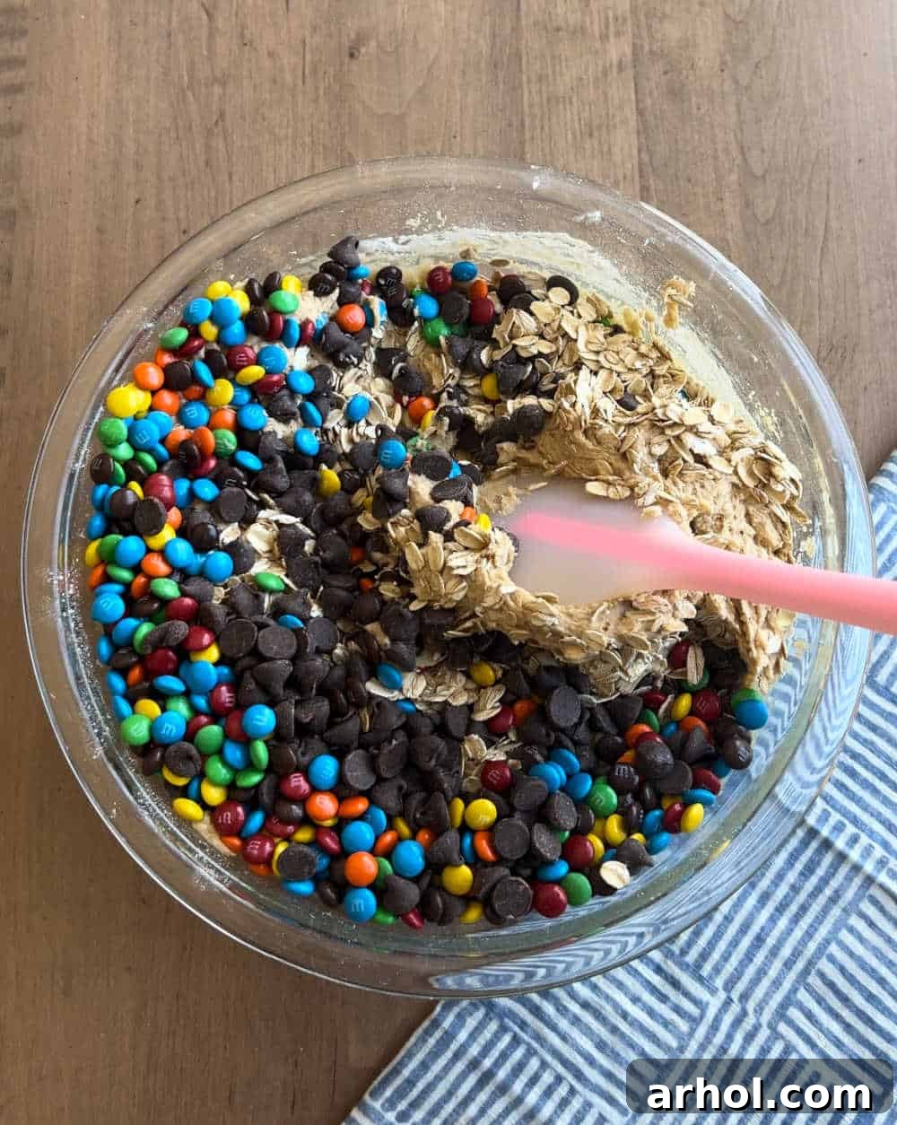 Mixing in oats, chocolate morsels, and M&M candies into the monster cookie dough with a spatula.