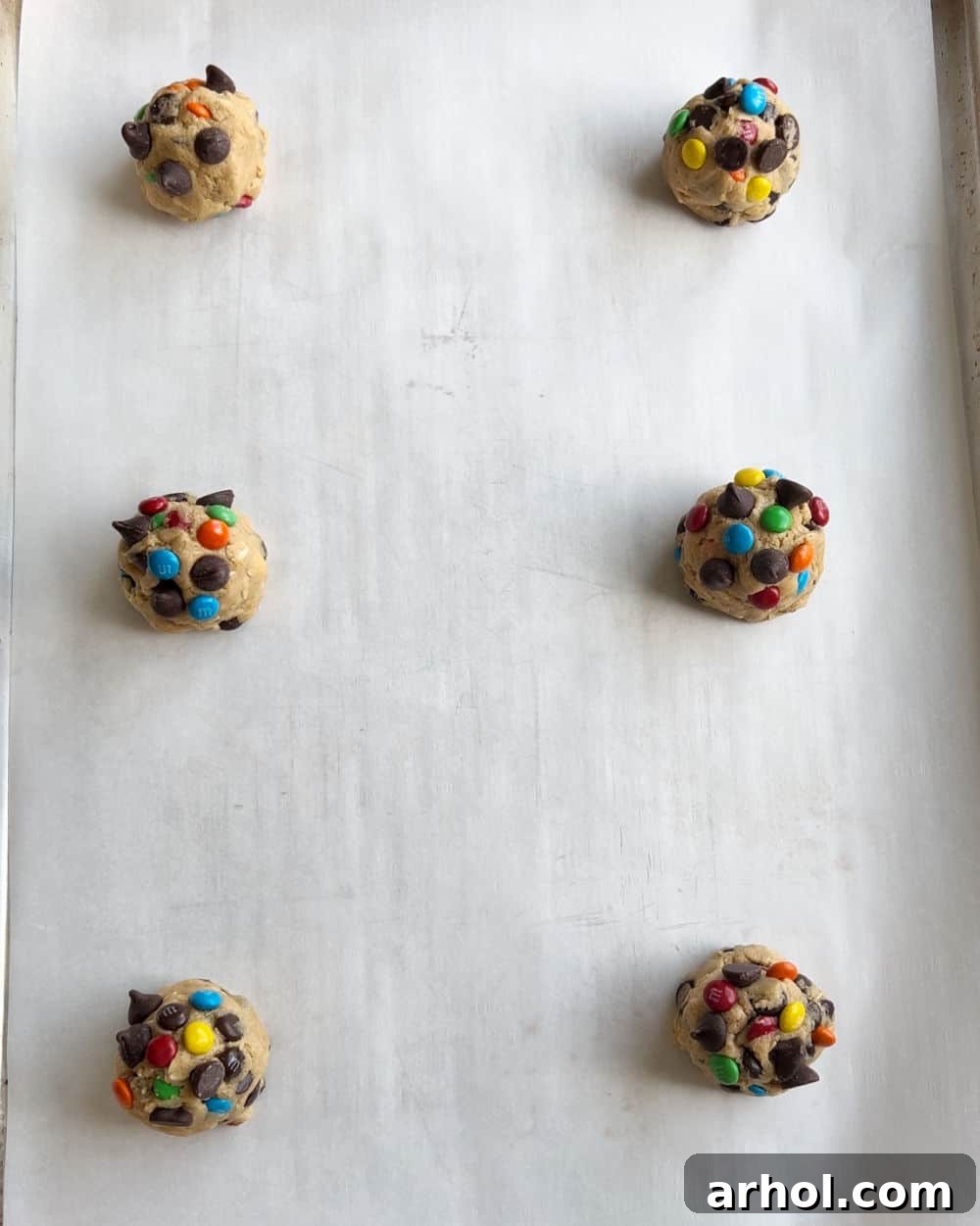 Scooped monster cookie dough balls perfectly arranged on a parchment paper-lined baking sheet, ready for chilling and baking.
