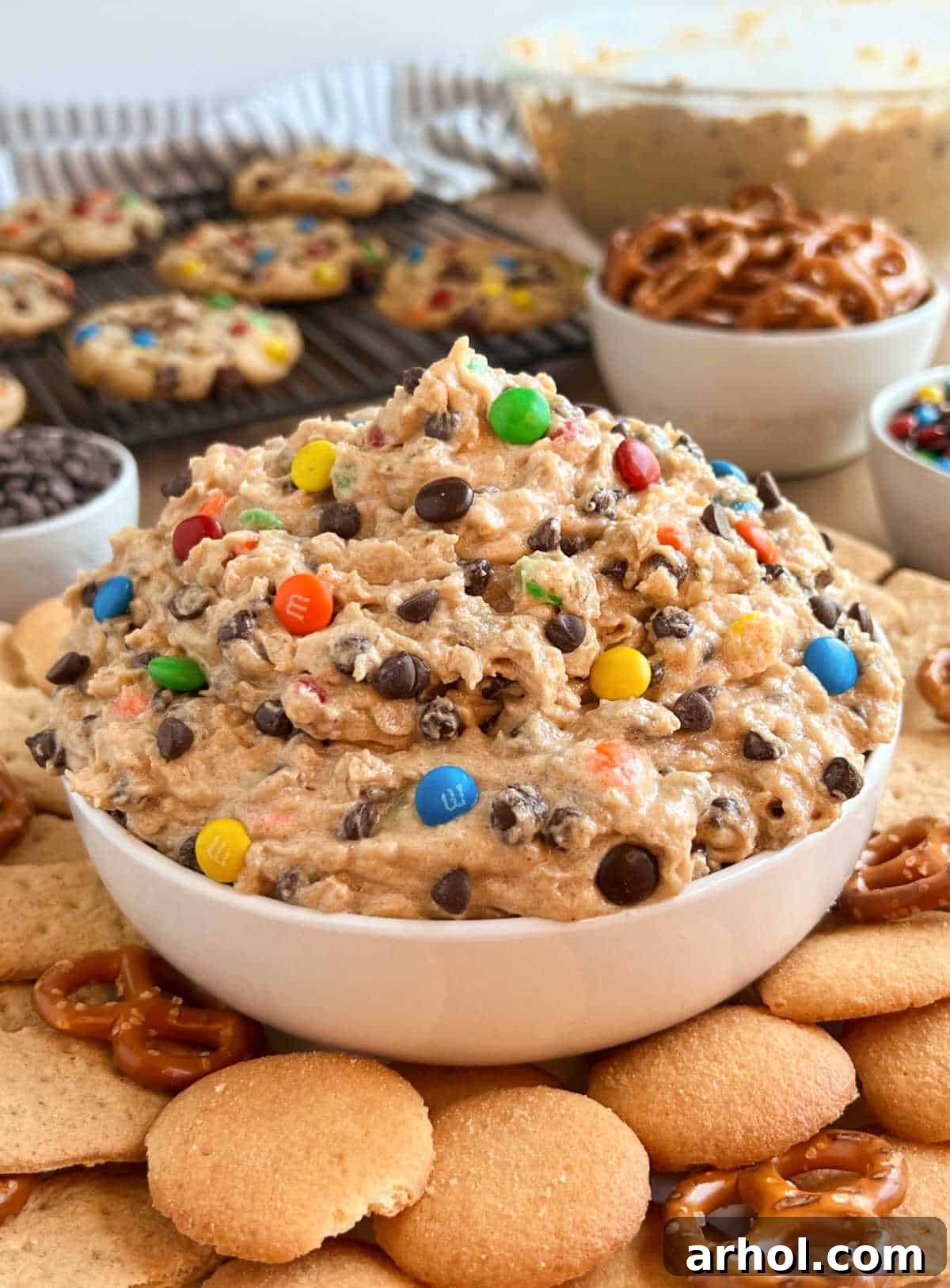 A vibrant bowl of Monster Cookie Dough Dip, brimming with colorful M&M's and chocolate chips, surrounded by an assortment of dippers like pretzels and actual monster cookies, ready for a party.