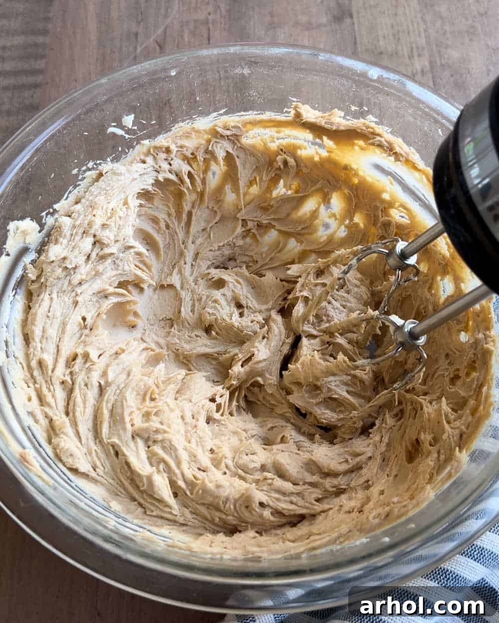 Close-up shot of butter and peanut butter being creamed together in a mixing bowl, creating a smooth, light brown mixture.
