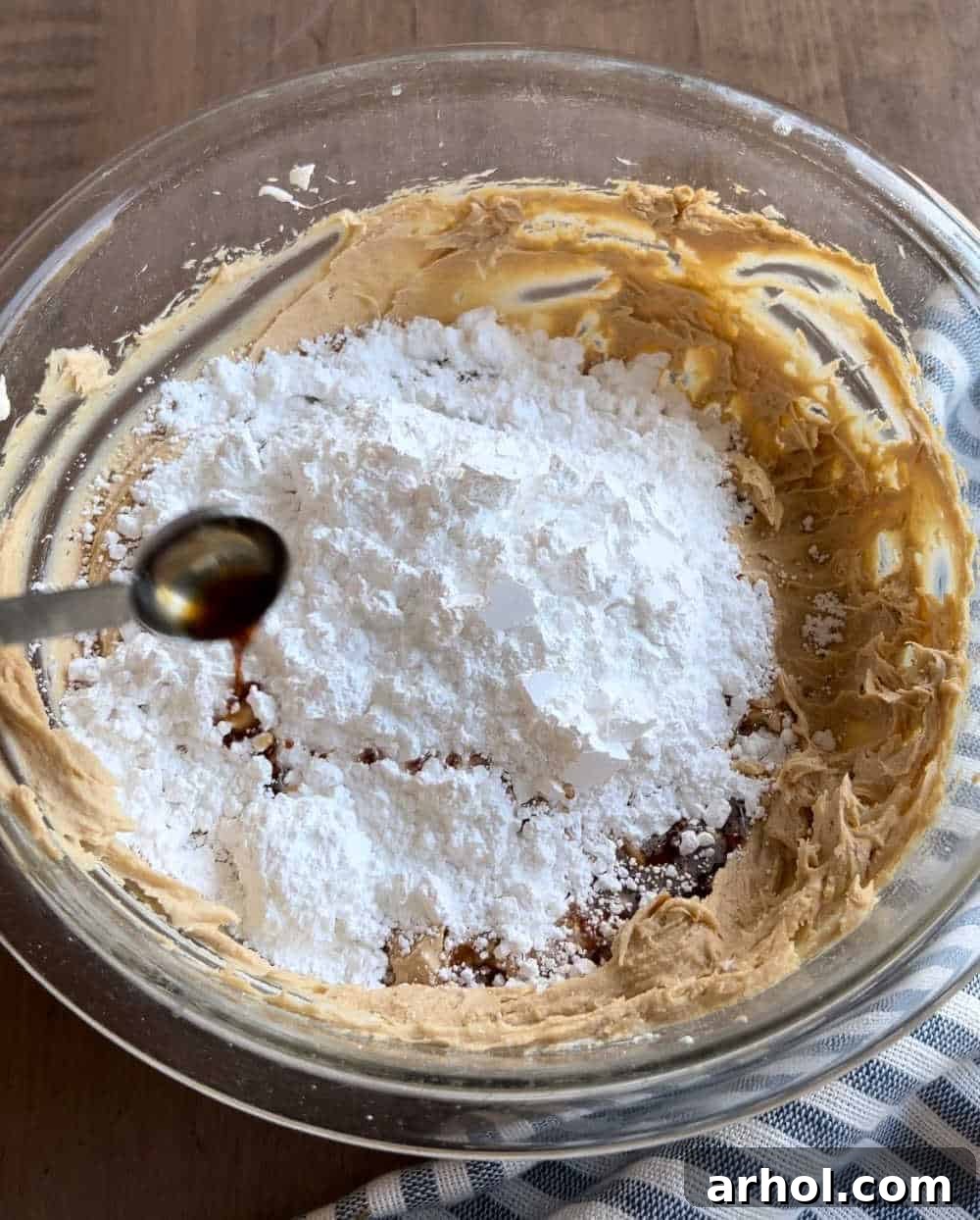 Adding powdered sugar and vanilla extract to the creamy mixture in a mixing bowl, prior to final mixing.