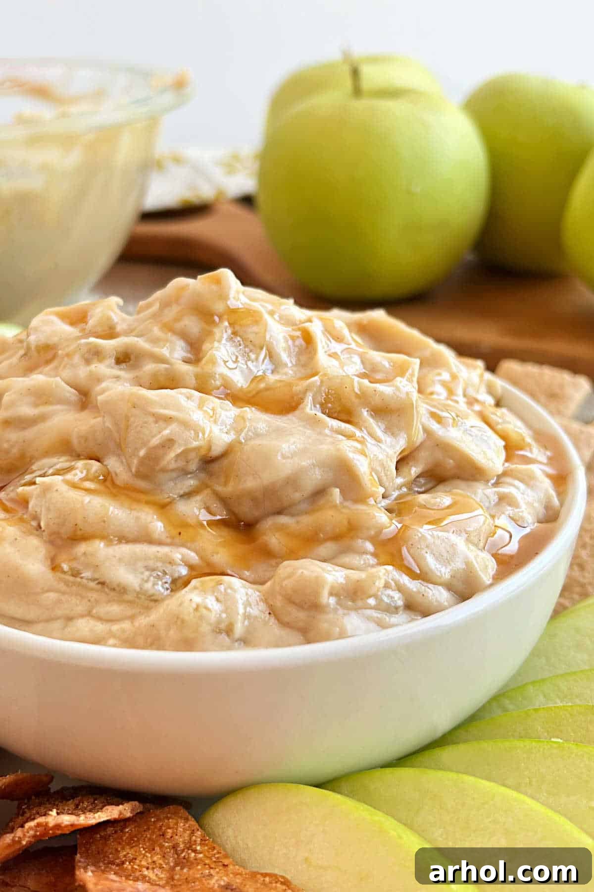 A beautifully presented bowl of creamy apple pie dip, garnished with a sprinkle of cinnamon and served alongside crisp fresh apple slices and crunchy cinnamon sugar chips, inviting you to indulge in the perfect fall dessert.