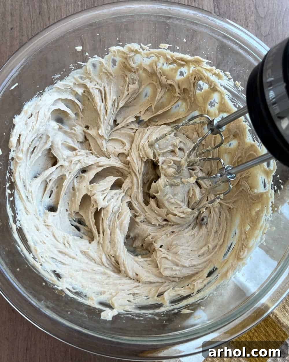 A close-up view of softened cream cheese, brown sugar, and vanilla extract being creamed together in a pristine white mixing bowl using an electric mixer, resulting in a beautifully smooth and unified base for the apple pie dip.