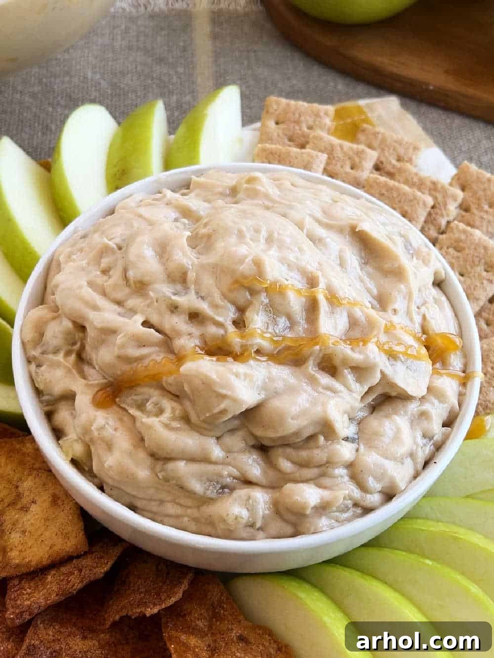 A close-up shot of a hand elegantly drizzling rich, golden caramel sauce over the meticulously prepared apple pie dip, which sits ready in a stylish serving bowl, enhancing both flavor and visual appeal.