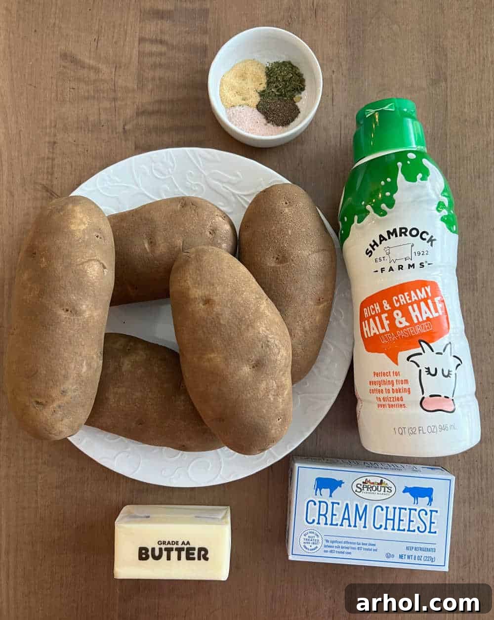 Fresh Russet potatoes, half and half, a block of cream cheese, butter sticks, and various seasonings laid out on a table, ready for mashing.