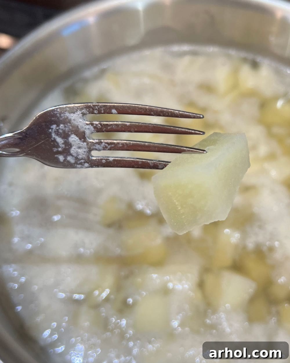 A fork easily piercing a boiled potato cube in a pot of water, indicating it's perfectly cooked for mashing.