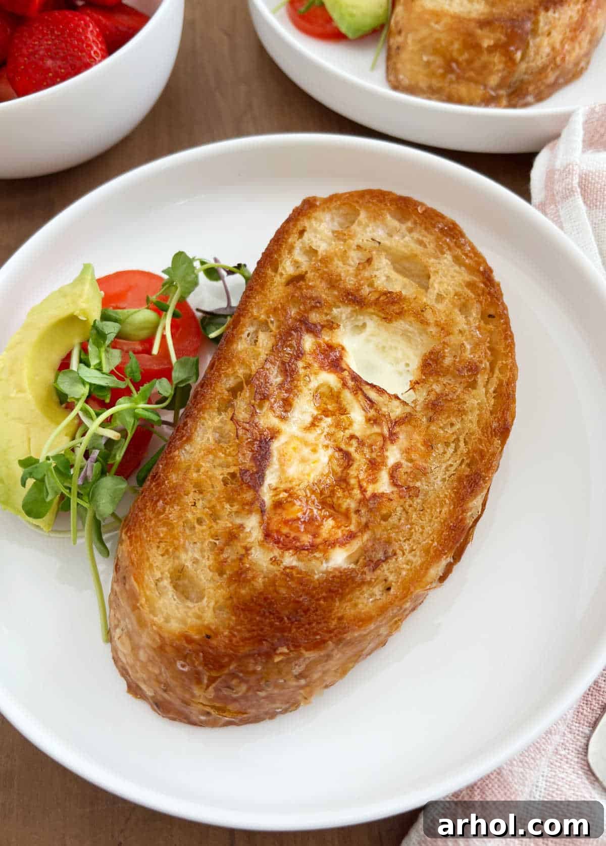 A perfectly cooked egg in a hole, served on sourdough toast with fresh garnishes on a white plate.
