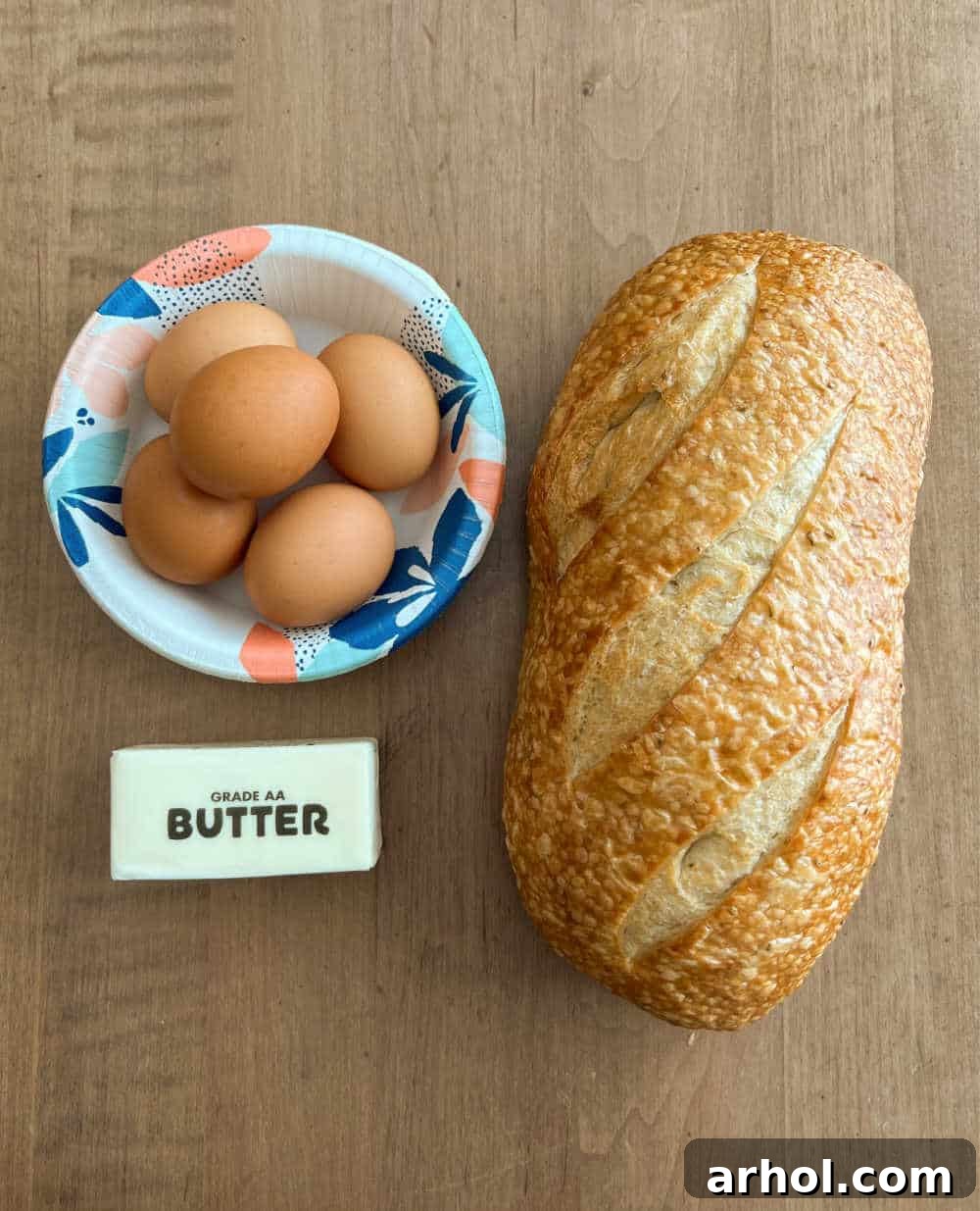 Fresh eggs, a stick of butter, and a rustic loaf of bread on a kitchen counter, ready for making egg in a hole.