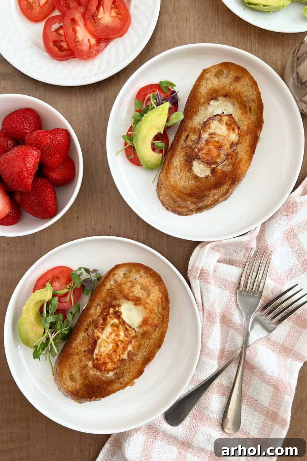 Plates of egg in a hole with various toppings like avocado and tomato, arranged on a breakfast table.