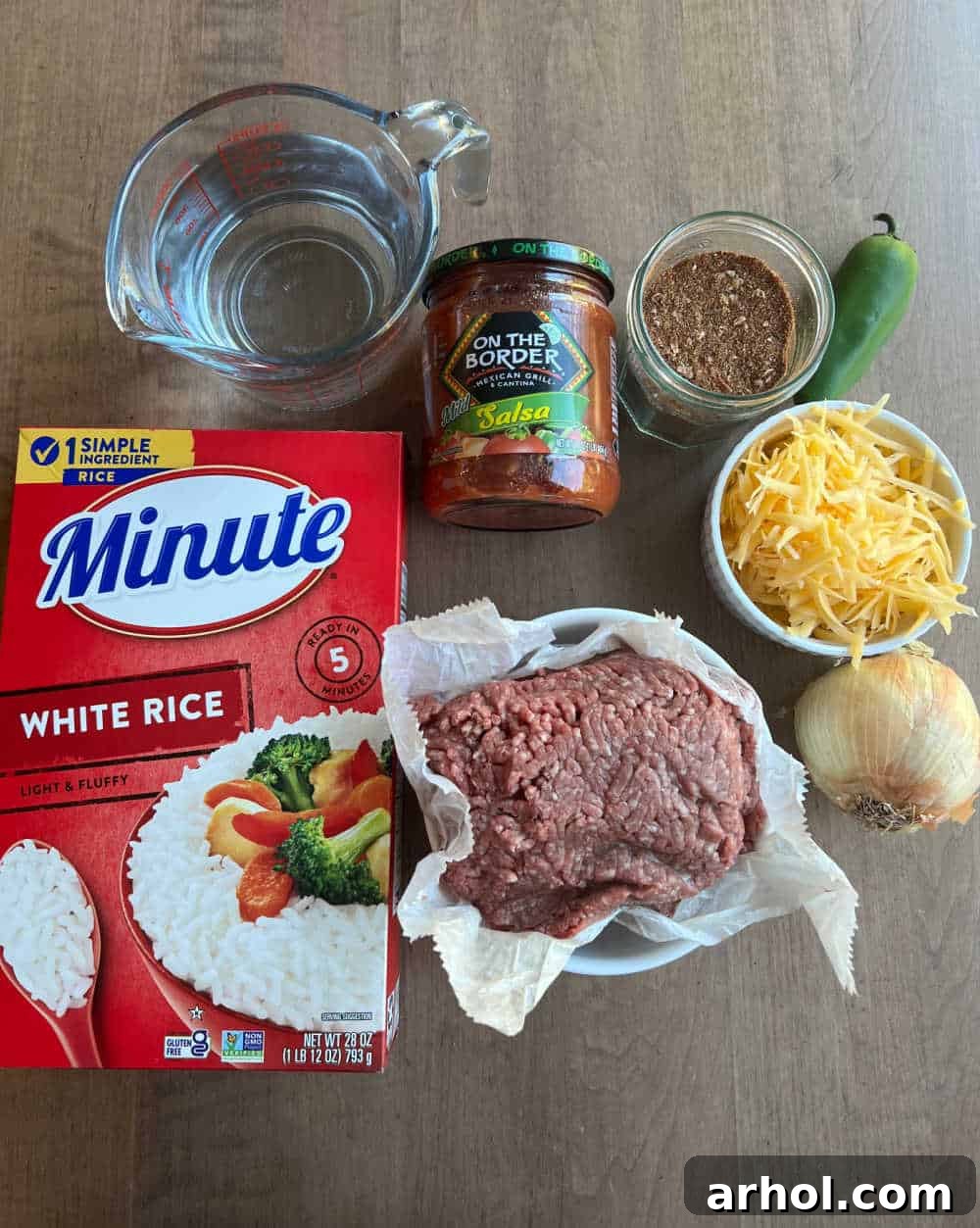 A colorful array of ingredients for taco rice laid out: ground beef, quick-cooking rice, water, salsa, shredded cheese, taco seasoning, diced onion, and sliced jalapeño pepper.