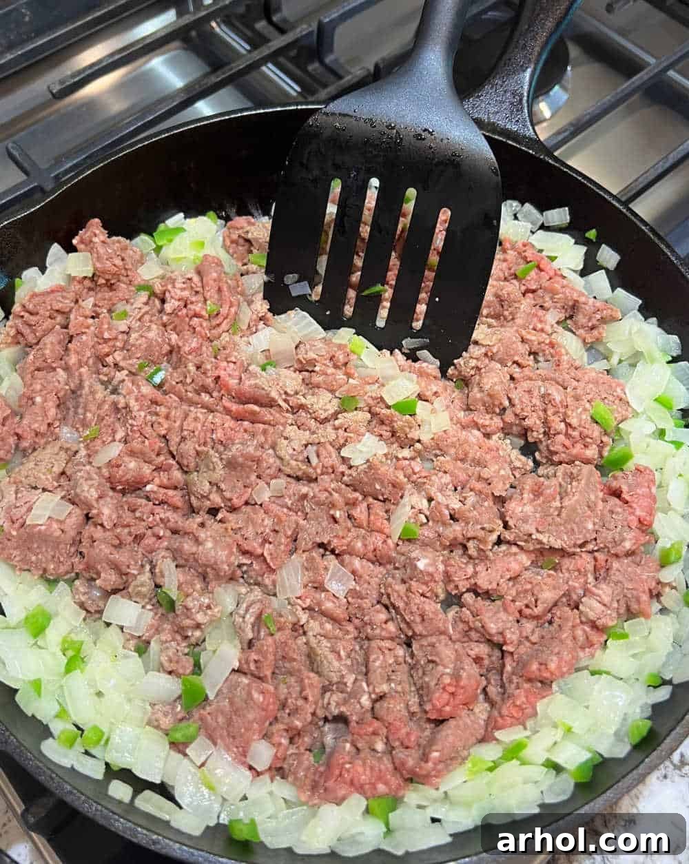 Ground beef, onion, and jalapeño cooking in a large cast iron skillet, browning evenly.
