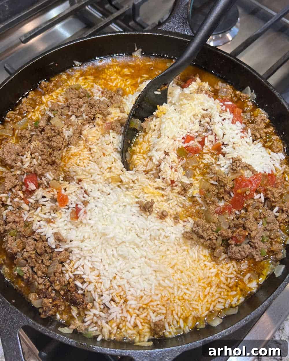 A large skillet showing ground beef, rice, and salsa being stirred together before cooking.