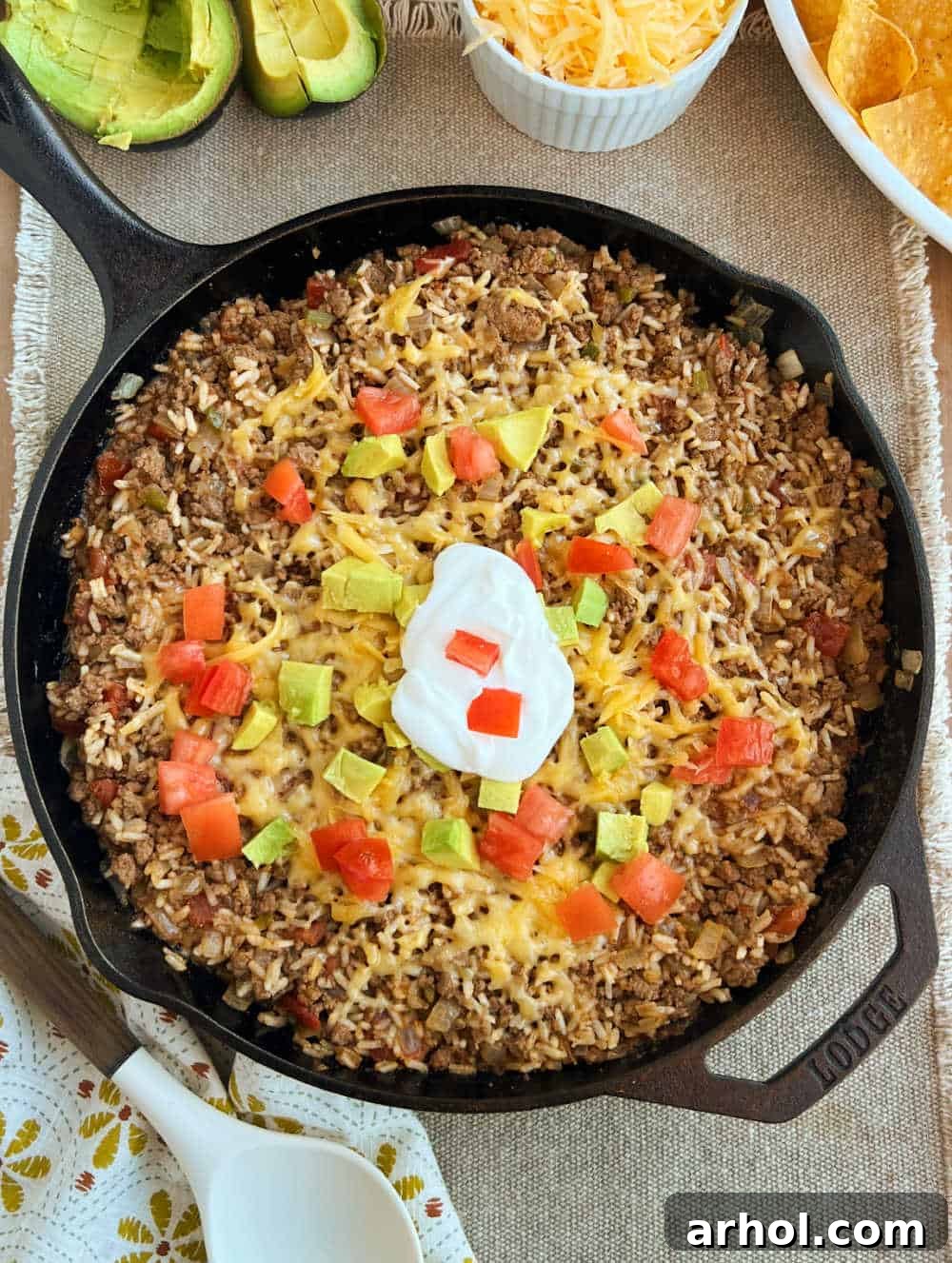 A vibrant cast iron skillet filled with cheesy taco rice, generously topped with fresh diced tomatoes and creamy avocado slices, ready to be served.