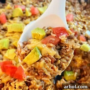 Serving of cheesy taco rice with ground beef in a spoon.
