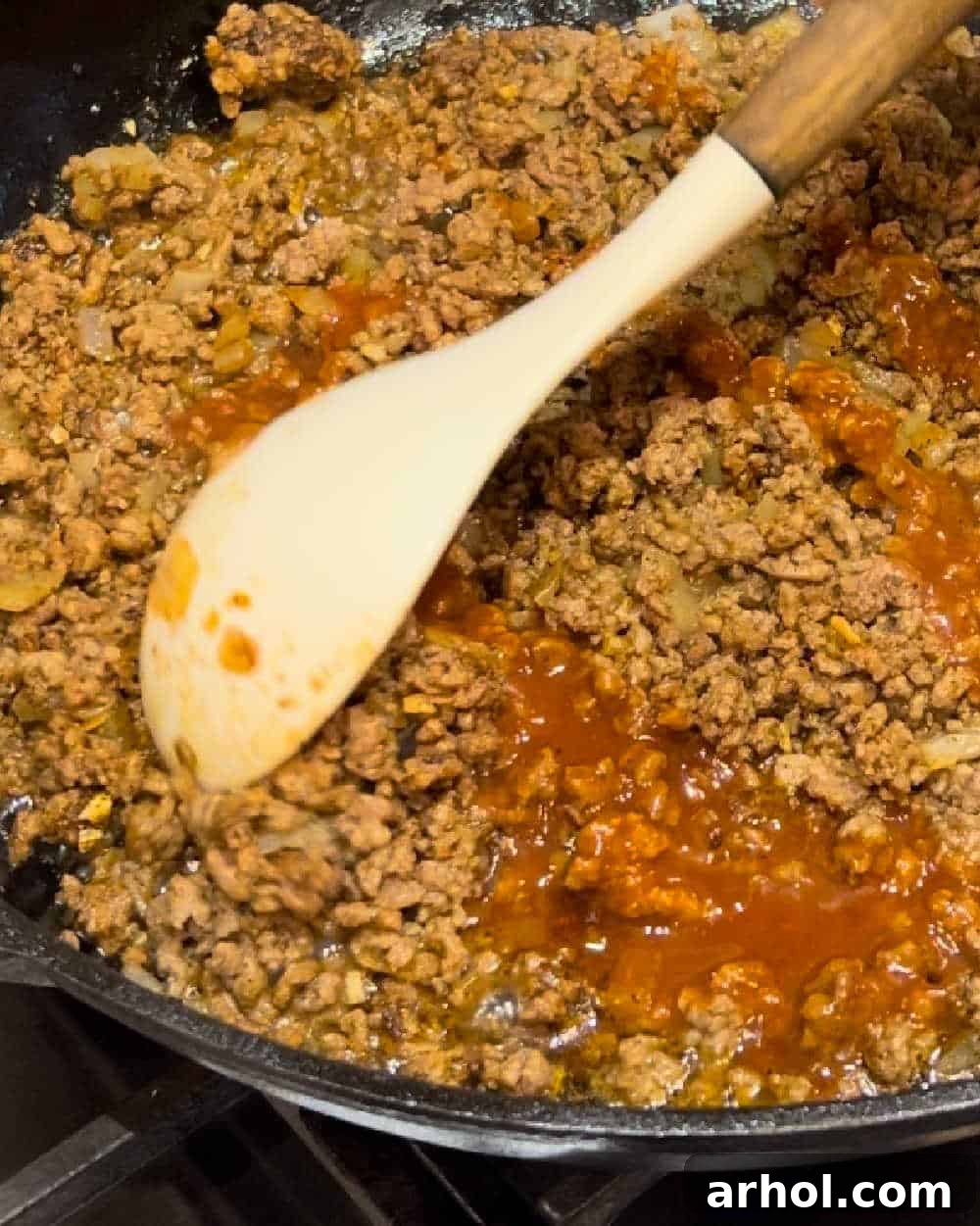 Stirring ground beef mixture with taco seasoning and a bit of enchilada sauce in a skillet.