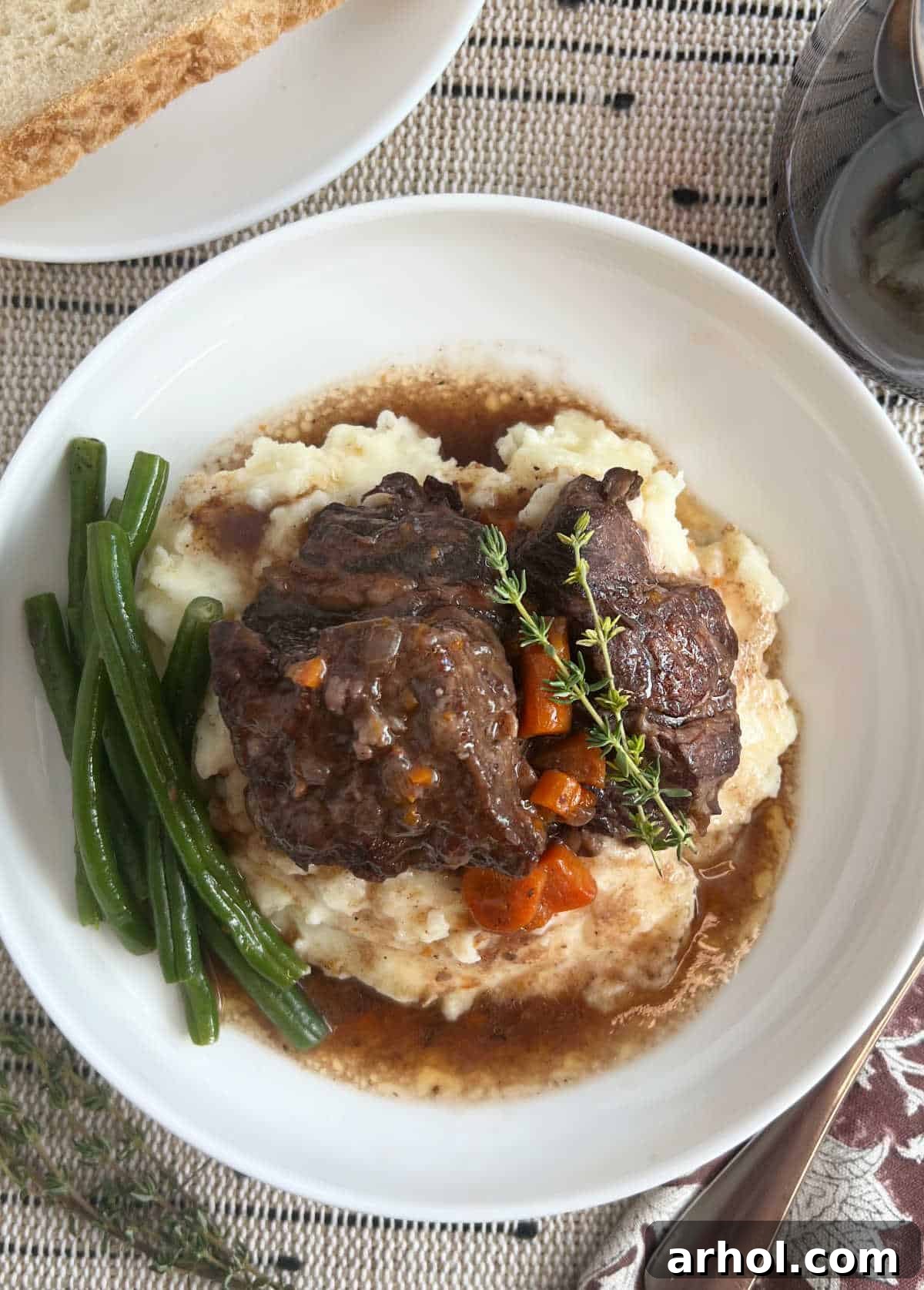 Melt-In-Your-Mouth Braised Short Ribs 2 plate of braised short ribs with carrots, green beans and mashed potatoes on table.