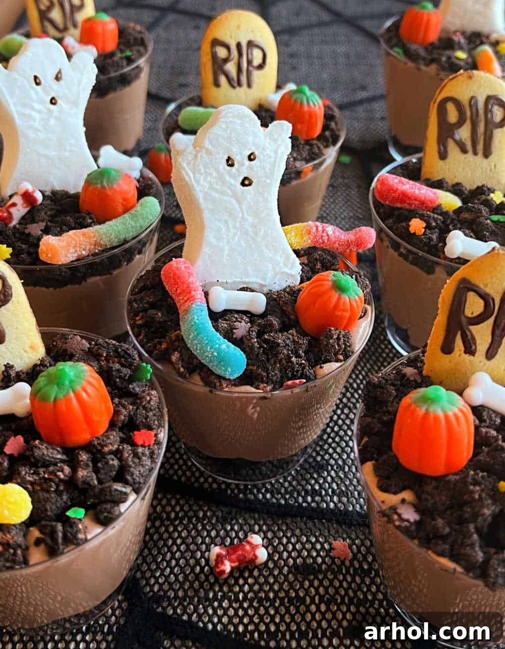 Quick Spooky Dirt Cups 7 Finished graveyard pudding cups decorated with tombstones, marshmallow ghosts, and gummy worms, displayed on a Halloween dessert table.