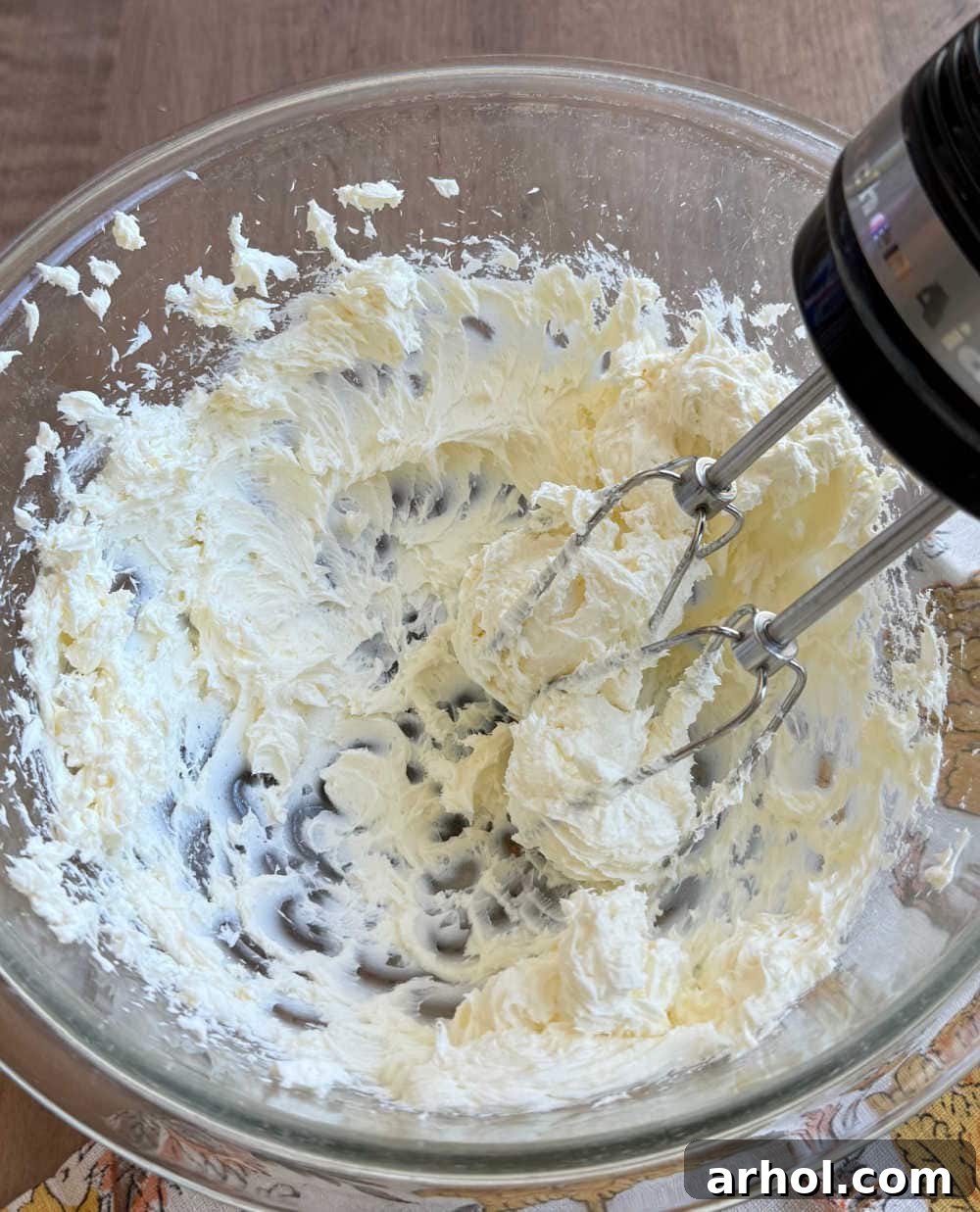 Beating softened cream cheese with an electric hand mixer for a smooth consistency.