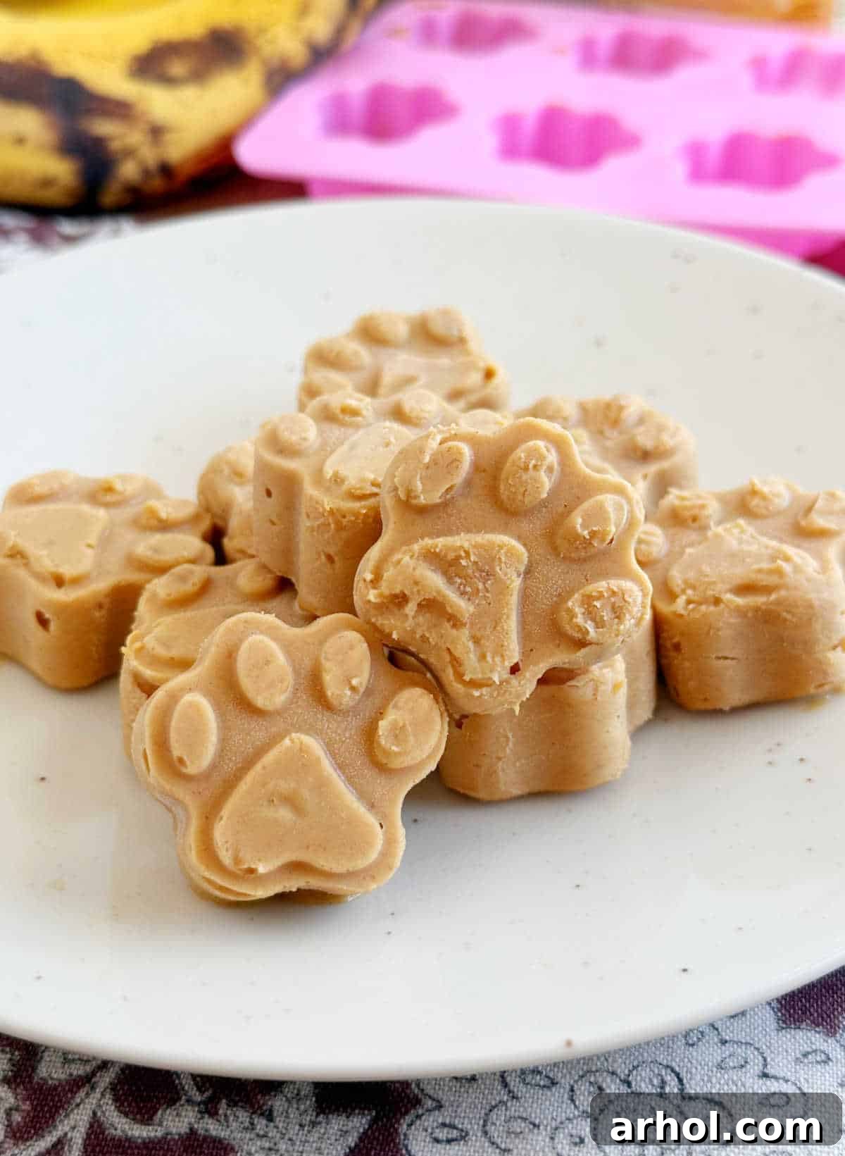 Homemade frozen peanut butter banana dog treats shaped like paw prints on a plate, ready to be enjoyed by pets.