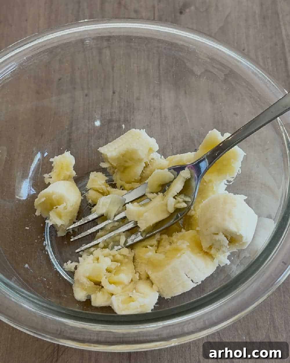 Mashing a ripe banana with a fork in a mixing bowl.