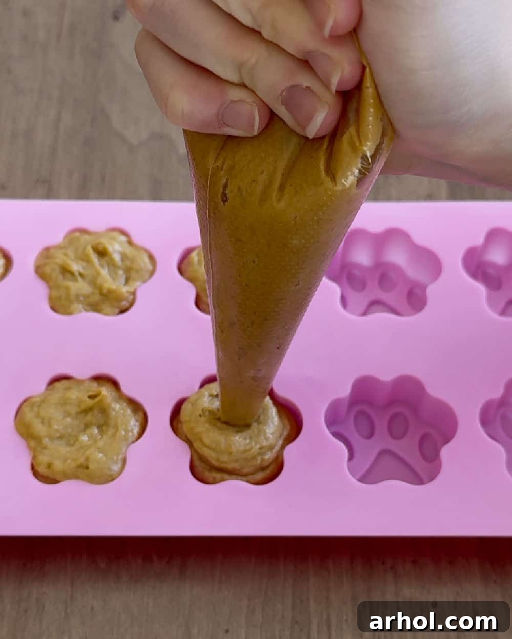 Piping the peanut butter, banana, and pumpkin mixture into paw print molds using a piping bag.