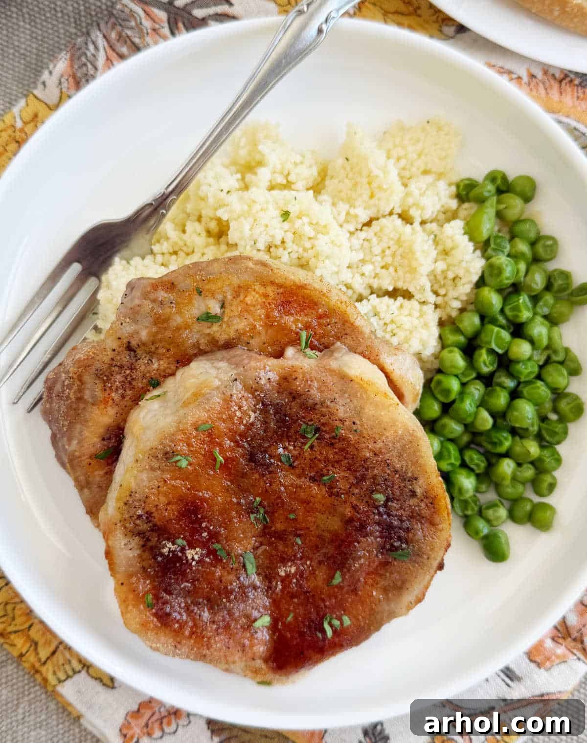 Brown Sugar Glazed Baked Pork Chops 2 Juicy baked brown sugar pork chops served with fluffy couscous and vibrant green peas on a crisp white plate, ready for a delicious family dinner.
