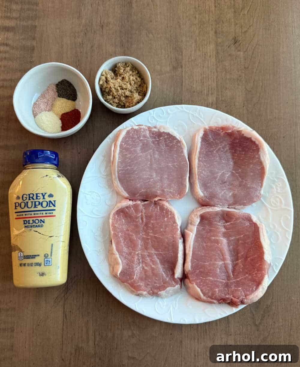 Brown Sugar Glazed Baked Pork Chops 3 Close-up view of essential ingredients for brown sugar pork chops: raw boneless pork chops, a small bowl of Dijon mustard, and a mix of brown sugar and spices.