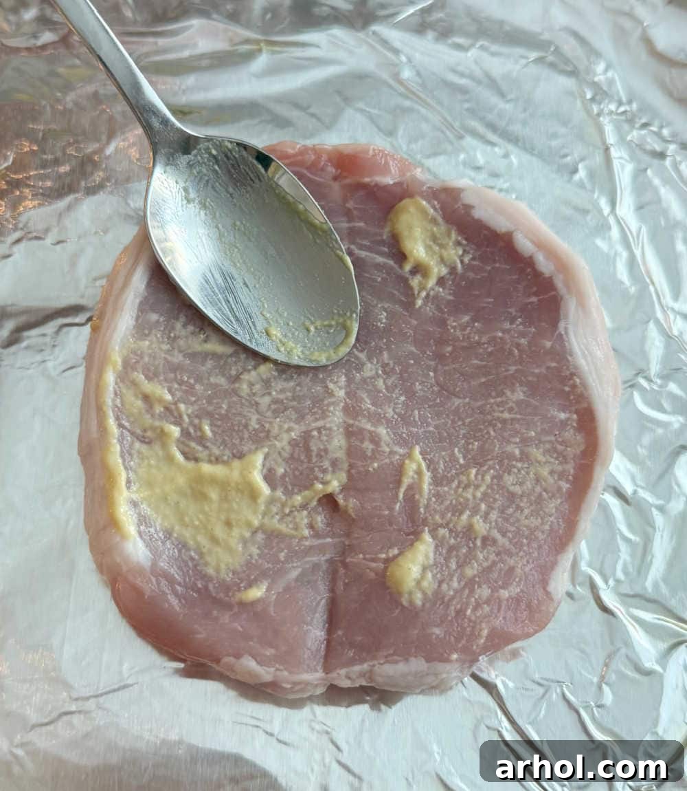 Brown Sugar Glazed Baked Pork Chops 5 Step 2: Spreading a thin layer of Dijon mustard evenly over pork chops.