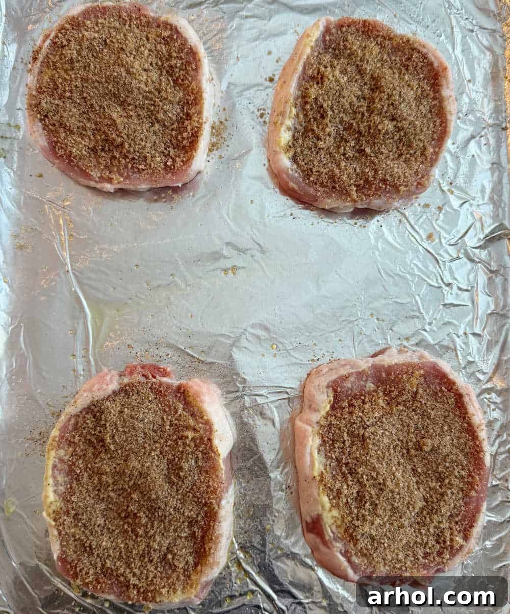 Brown Sugar Glazed Baked Pork Chops 6 Step 3: Seasoned pork chops covered with a brown sugar and spice rub on a baking sheet, ready for the oven.