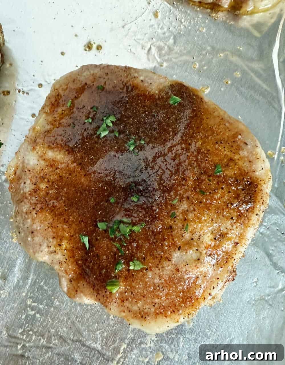 Brown Sugar Glazed Baked Pork Chops 7 Step 4: A perfectly baked brown sugar pork chop, garnished with fresh parsley, showcasing its golden-brown crust.