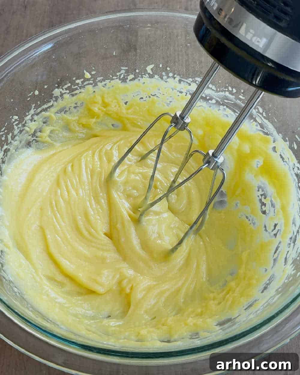 A close-up of a hand using an electric mixer to thoroughly combine the pudding and milk mixture until smooth and creamy.