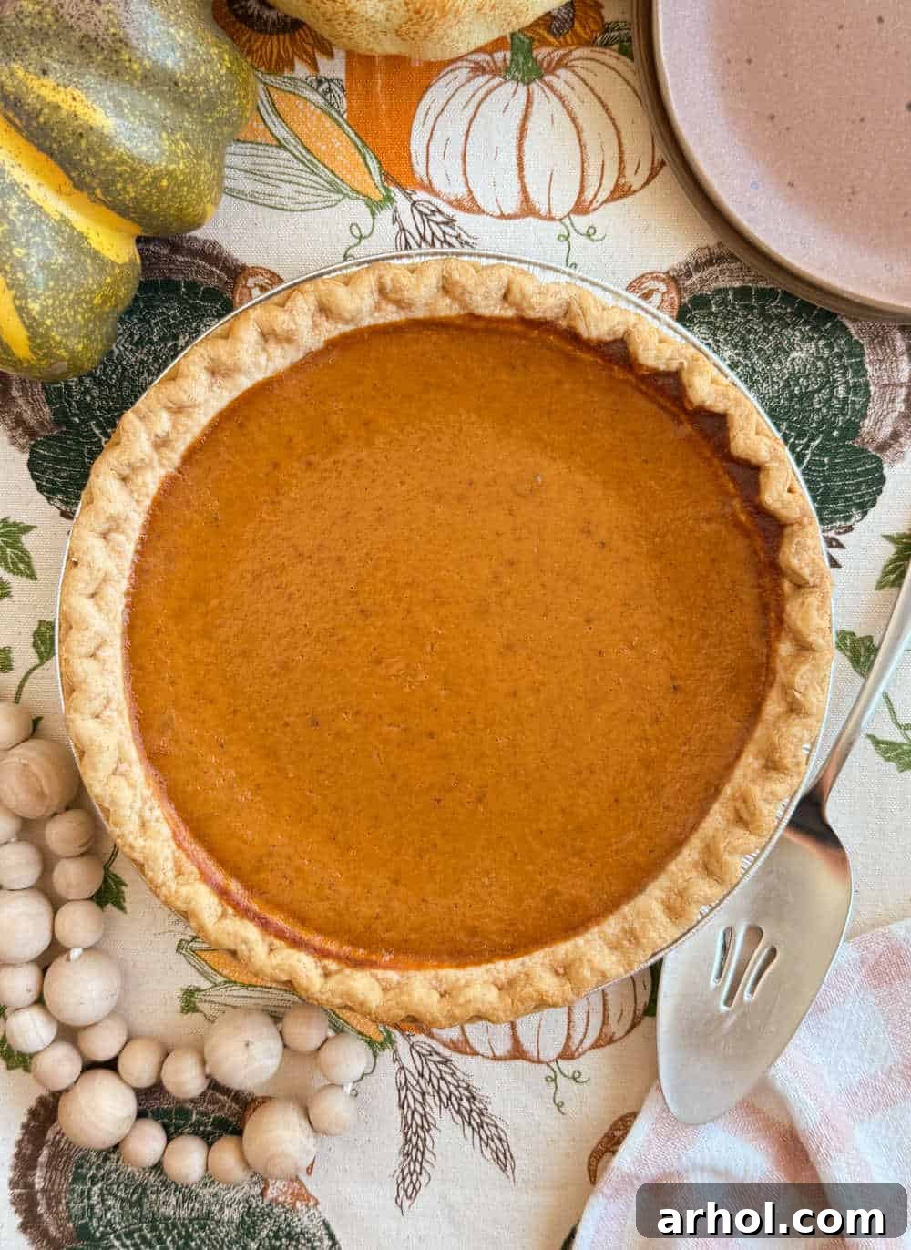 A beautifully golden-brown homemade pumpkin pie sitting on a rustic wooden table, surrounded by other Thanksgiving decorations, waiting to be sliced and served.
